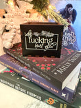 Load image into Gallery viewer, Black, wooden box with “who fucking hurt you” printed on the front. Books and a Christmas tree in the background