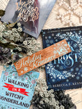 Load image into Gallery viewer, Woodgrain Thin Horizontal Sign with light blue text that reads "Holiday Romance" surrounded by blue snowflakes and a bookstack. © FireDrake Aristry 2024