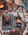 Load image into Gallery viewer, A decorative tarot card shelf sign featuring the card 'The Shield Maiden' with artwork depicting a female figure on the left, A decorative tarot card shelf sign featuring the card 'The Forehand" with artwork depicting a male figure on the right, surrounded by various items like books, a vase, and decorative items.