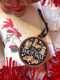 Load image into Gallery viewer, Round, wooden ornament with a navy blue background and dark woodgrain frame. Featuring text that reads "Merry Smut-mas" surrounded by gingerbread men and women in smutty positions. ©FireDrake Artistry 2024.