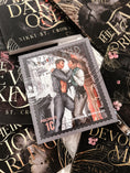 Load image into Gallery viewer, A postage stamp with two men embraced titled "Everland", atop a book collection of black books