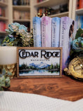 Load image into Gallery viewer, Wooden sign with mountain and lake scene. "Cedar Ridge Washington" printed on the top of the sign. Books, flowers. and teacup in the background.