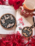 Load image into Gallery viewer, Round, wooden sign and ornament, each with a navy blue background and dark woodgrain frame. Featuring text that reads "Merry Smut-mas" surrounded by gingerbread men and women in smutty positions. ©FireDrake Artistry 2024.