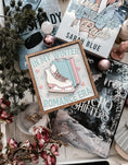 Load image into Gallery viewer, A wooden sign with a white background and woodgrain frame displaying the phrase 'IN MY WINTER ROMANCE ERA' surrounded by winter-themed illustrations such as a ice skate, snowflakes, and hearts. © FireDrake Artistry 2024