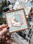 Load image into Gallery viewer, A wooden sign with a white background and woodgrain frame displaying the phrase 'IN MY WINTER ROMANCE ERA' surrounded by winter-themed illustrations such as a ice skate, snowflakes, and hearts. © FireDrake Artistry 2024