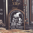Load image into Gallery viewer, Cozy Reader Ghosty Sign. Black background with a dark wood border with a white design engraved.
Featuring a ghost reading a book and wearing a witch hat, surrounded by flowers and a pumpkin. Text above reads “Books. Coffee. Sweaters. Cats.” While the text below reads “Cozy Reader Book Club.”