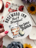 Load image into Gallery viewer, Round sign with "Rosewood Inn Bed and Breakfast" and a glass or whisky with a lime wedge on it. Books and trinkets in the background.