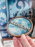 Load image into Gallery viewer, Round wooden sign with 'MOONBEAM' text and dragon design held in hand.