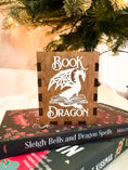Load image into Gallery viewer, Wooden box with 'Book Dragon' design on top of books with a Christmas tree in the background