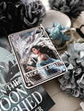 Load image into Gallery viewer, A 'Moonplume' Tarot Card featuring an illustration of a dragon ad a woman, placed next to the book 'When the Moon Hatched' by Sarah A. Parker, with a decorative background.