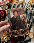Load image into Gallery viewer, A decorative shelf sign featuring the 'The Future King' tarot card from the Blood and Ash series being held in a hand, with books and decorative elements in the background.
