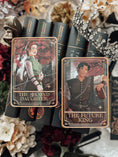 Load image into Gallery viewer, A decorative shelf sign featuring the 'The Future King' tarot card on the right, and "The Second Daughter" tarot card on the left, from the Blood and Ash series, with a book stack, crown, and decorative elements in the background.