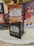 Load image into Gallery viewer, Wooden and black boxes with printed design with 'Just one more chapter' text and a book stack with flowers, against a physical books and Christmas tree background.