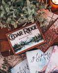 Load image into Gallery viewer, Wooden sign with mountain and lake scene. "Cedar Ridge Washington" printed on the top of the sign. Books, flowers. and teacup in the background.