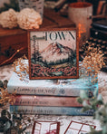 Load image into Gallery viewer, Sign with "Small Town Romance" and a mountain with trees and a lake printed on it. Books and flowers in the background.