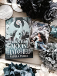 Load image into Gallery viewer, A 'Moonplume' Tarot Card featuring an illustration of a dragon ad a woman, placed next to the book 'When the Moon Hatched' by Sarah A. Parker, with a decorative background.