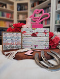 Load image into Gallery viewer, Sign with Chestnut Springs book titles and boots with flowers printed on it. Books and flowers in the background.