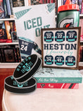 Load image into Gallery viewer, Sign that says "Heston University" with blue hockey jerseys on it. Books and trinkets int eh background.