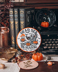 Load image into Gallery viewer, Dead Set on Reading Sign - Orange. White round sign with a skeleton lounging and reading a book surrounded by pumpkins.