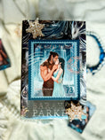 Load image into Gallery viewer, A postage stamp featuring artwork of a romantic scene on top of a book cover with decorative elements on a textured background