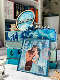 Load image into Gallery viewer, Decorative box with blue and white design, featuring a book cover and 'Moonbeam' label.A postage stamp featuring artwork of a romantic scene.
