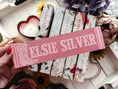 Load image into Gallery viewer, Wooden sign with Elsie Silver and a boot printed on it. Sign is held in a hand with books and flowers in the background.
