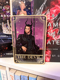 Load image into Gallery viewer, Tarot Card titled "The Devil" with an image of a man with horns in a suit on a bookshelf with books in the background.