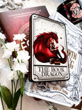 Load image into Gallery viewer, Tarot Card titled "The Book Dragon" with an image of a girl reading a book with a red dragon, , on top of a stack of books with flowers in the background.