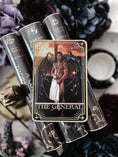Load image into Gallery viewer, Tarot Card titled "The General" with a single, shirtless man printed on the card, on top of a stack of books with flowers and bookish trinkets in the background.