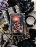 Load image into Gallery viewer, Tarot Card titled "The Shadowsinger" with a single, shirtless man printed on the card, on top of a stack of books with flowers and bookish trinkets in the background.
