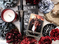 Load image into Gallery viewer, Tarot Card titled "The General" with a single, shirtless man printed on the card, on top of a stack of books with flowers and bookish trinkets in the background.