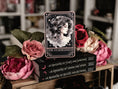 Load image into Gallery viewer, A Tarot Card "The Starblessed" with an image of a celestial woman printed on it on top of a book stack from the series A Kingdom of Stars and Shadows by Holly Renee with flowers and other books in the background.