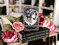 Load image into Gallery viewer, A Tarot Card "The Starblessed" with an image of a celestial woman printed on it on top of a book stack from the series A Kingdom of Stars and Shadows by Holly Renee with flowers and other books in the background.
