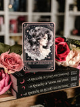 Load image into Gallery viewer, A Tarot Card "The Starblessed" with an image of a celestial woman printed on it on top of a book stack from the series A Kingdom of Stars and Shadows by Holly Renee with flowers and other books in the background.