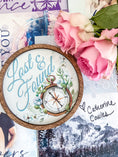 Load image into Gallery viewer, Round wooden sign with the words "Lost & Found" and a compass with flowers printed on it. Flowers and books in the background