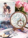 Load image into Gallery viewer, Round wooden sign with the words "Lost & Found" and a compass with flowers printed on it. Sign is placed on a wooden easel. Flowers and books in the background.