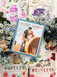 Load image into Gallery viewer, A postage stamp featuring artwork of a romantic scene, with a books and decorative flowers in the background.