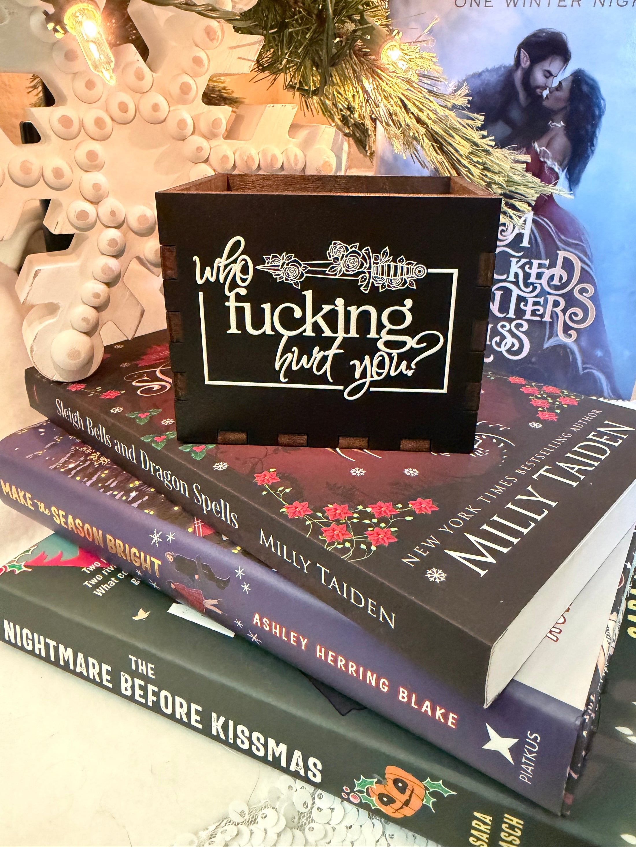 Black, wooden box with “who fucking hurt you” printed on the front. Books and a Christmas tree in the background 