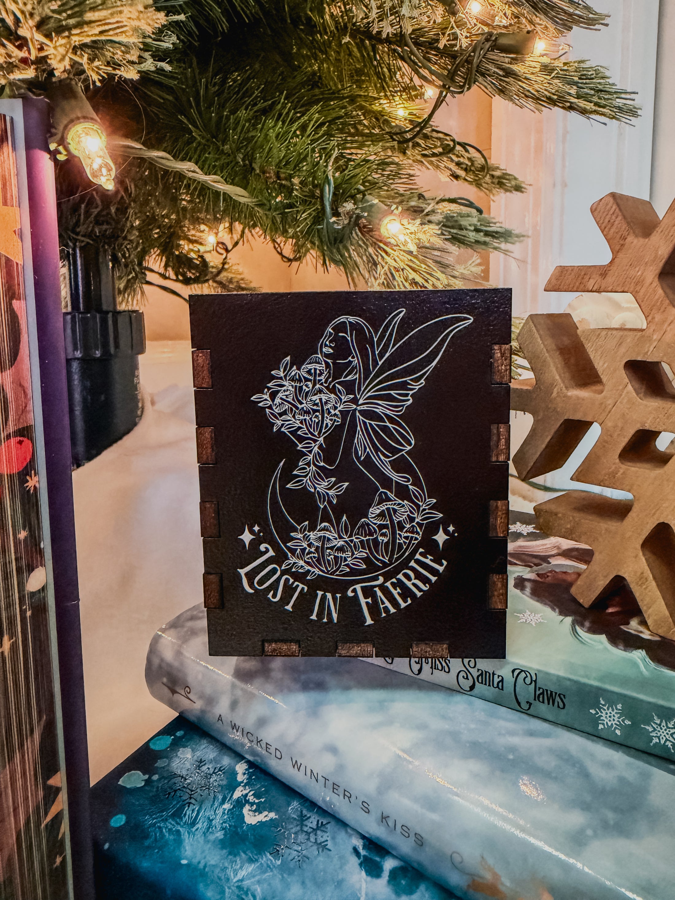 Black box with printed fairy design and 'Lost in Faerie' text, against a Christmas tree background.