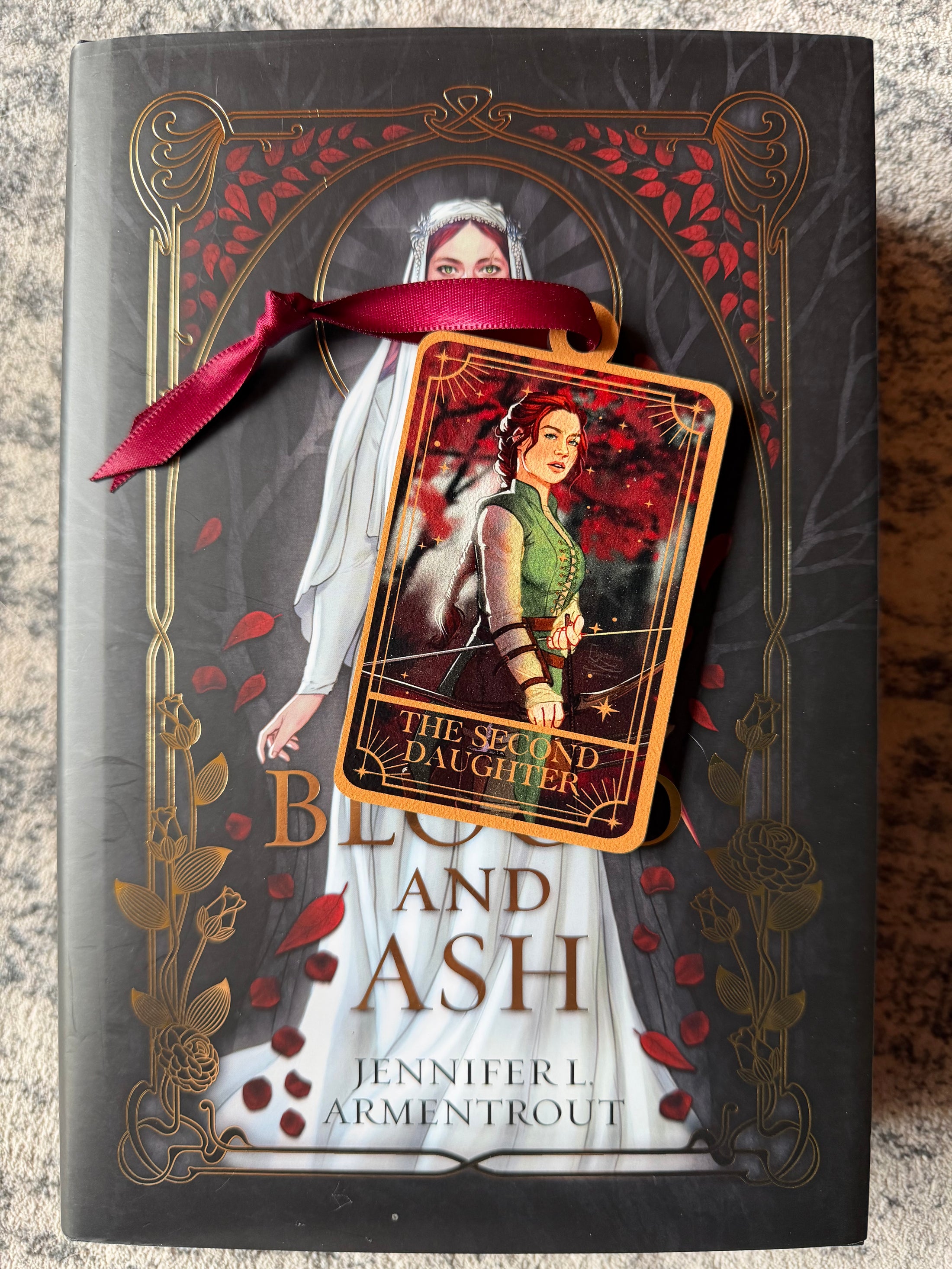 Tarot Card ornament titled "The Second Daughter" with  maroon ribbon and book underneath.