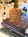 Load image into Gallery viewer, Wooden box with "Book Lover" printed on them. Bookstack and Christmas tree in the background. 
