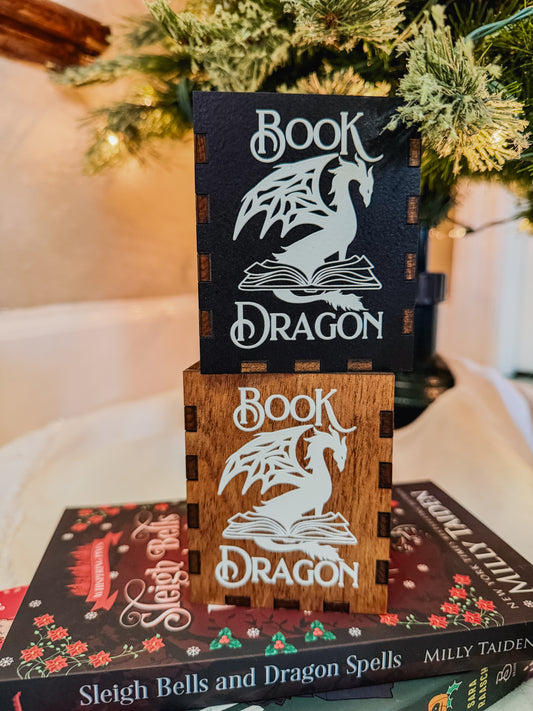 Decorative bookend with 'Book Dragon' design on top of a book titled 'Sleigh Bells and Dragon Spells' by Milly Taden.