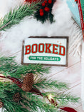 Load image into Gallery viewer, Decorative sign with a wooden frame that reads 'Booked for the Holidays' in red on a white background. © FireDrake Artistry 2025.
