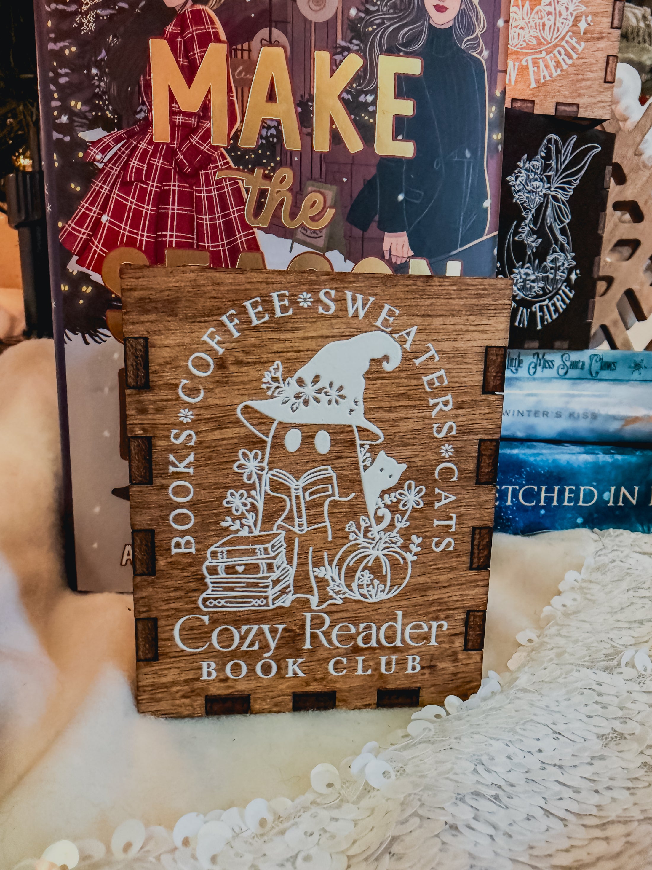 Wooden box with printed design with 'Cozy Reader' text and a ghost with books, against a book stack and Christmas tree background.