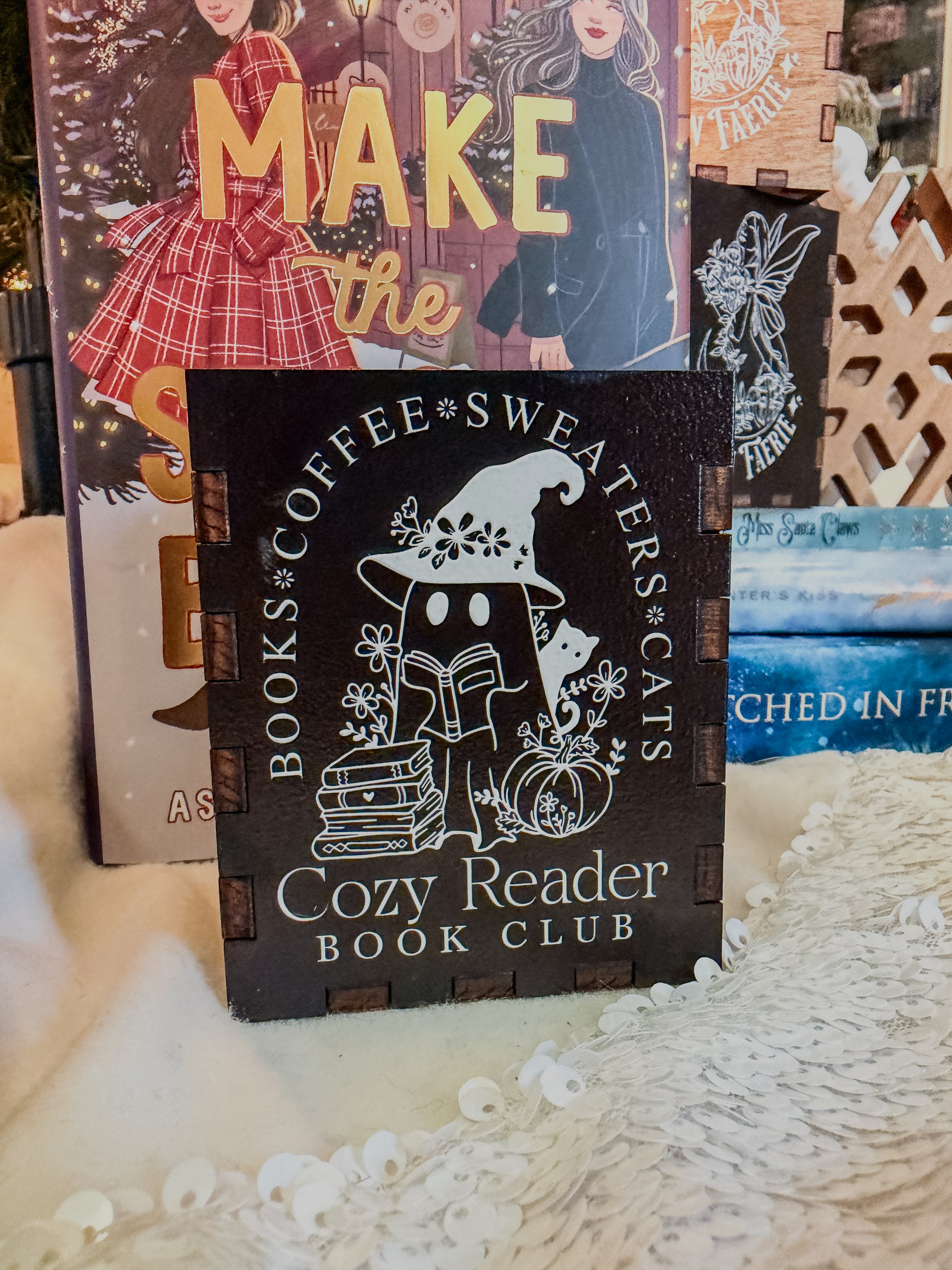 black box with printed design with 'Cozy Reader' text and a ghost with books, against a book stack and Christmas tree background.