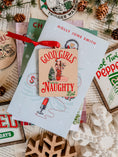 Load image into Gallery viewer, A rectangular wooden ornament featuring a Christmas tree of books next to a girl in a Santa hat tied up with Christmas lights surrounded by text that reads 'Good Girls Naughty List'. © FireDrake Artistry 2023

