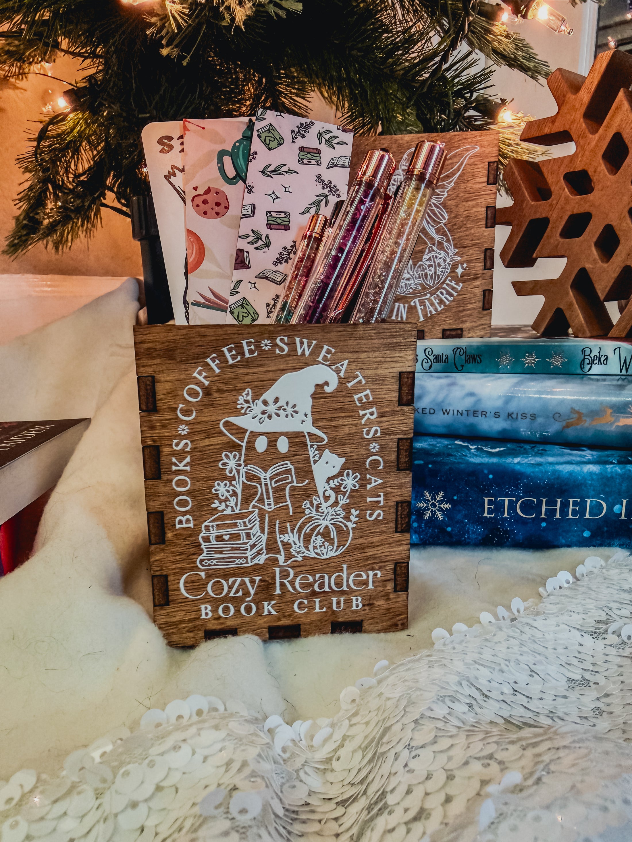 Wooden box with printed design with 'Cozy Reader' text and a ghost with books, against a book stack and Christmas tree background.