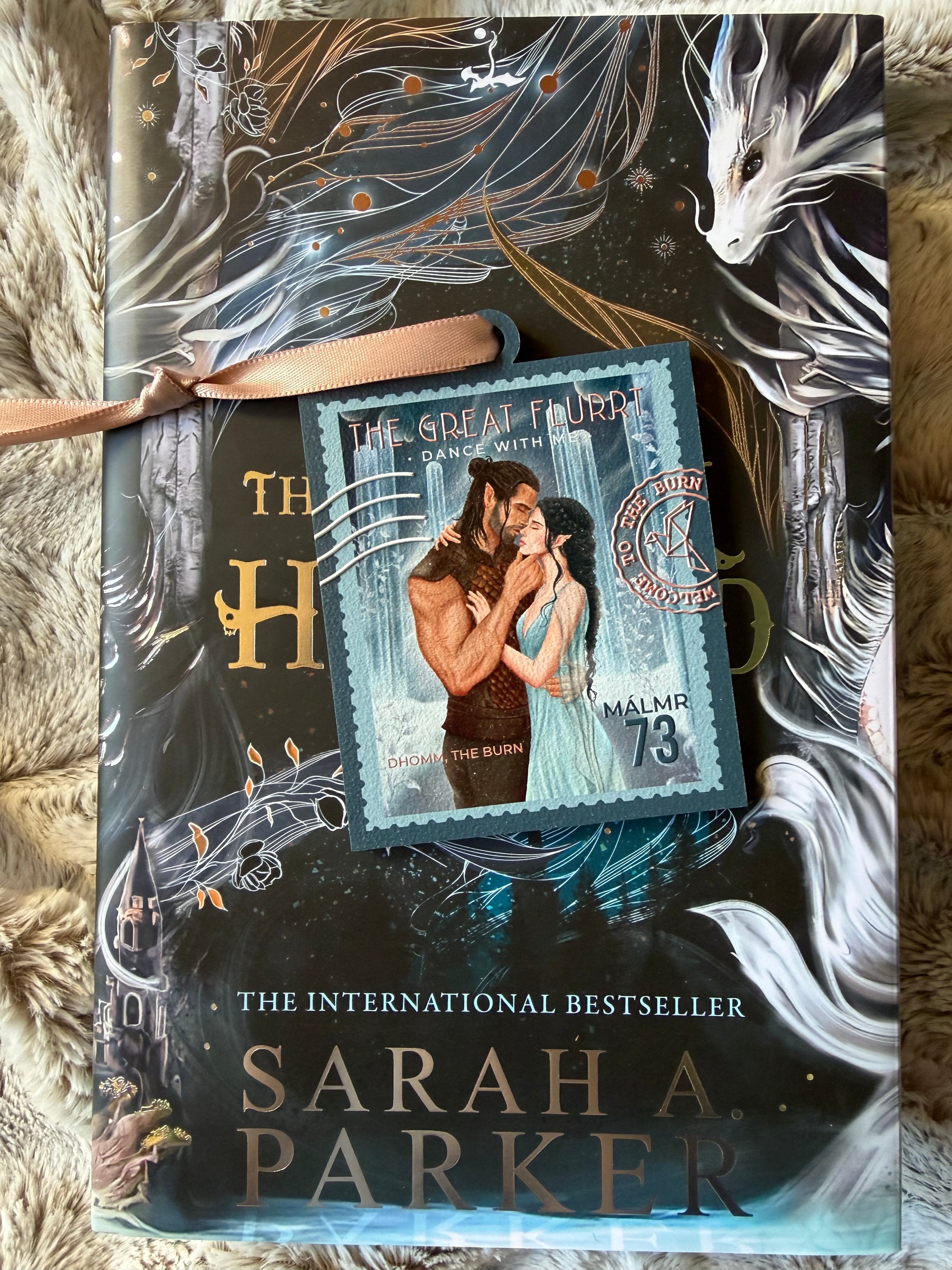 Stamp on ornament named "The Great Flurrt" with a pink ribbon and a book with a dragon in the background. 