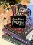 Load image into Gallery viewer, Black, wooden box with “who fucking hurt you” printed on the front. Books and a Christmas tree in the background 
