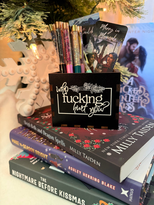Black, wooden box with “who fucking hurt you” printed on the front. Books and a Christmas tree in the background 